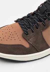 Bruna mocka- och lädersneakers med perforerade detaljer, svarta snören med vita accenter och en texturerad gummisula.