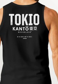 Schwarzes Tanktop mit fett gedrucktem weißen Text "TOKIO KANTO NEVERLESS" und Koordinaten sowie "JAPAN" am unteren Rand. Glatte Textur.