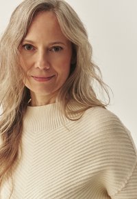 Kreemikreemiga kudum, millel on soonikkoes kaelus ja kalasabamuster. Mudelil on pikad, lainelised juuksed. Üksildane taust.