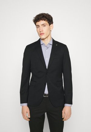 Schwarzer, taillierter Blazer mit Reverskragen, zwei Knöpfen und Taschen an den Seiten. Getragen über einem hellblauen, gemusterten Hemd. Glatte Stofftextur.