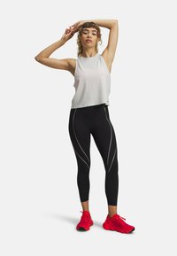 Lys grå ærmeløs træningstop med mesh detaljer, parret med sorte leggings med hvide diagonale striber og røde træningssko.
