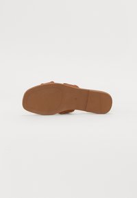 Brun sandal med en teksturert overflate, justerbare stropper og en flat gummisåle. Størrelse 38 er preget på bunnen.