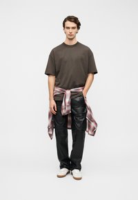 Καφέ κοντομάνικη μπλούζα, μαύρο δερμάτινο παντελόνι και κόκκινο-γκρι καρό πουκάμισο δεμένο στη μέση. Λευκά αθλητικά παπούτσια ολοκληρώνουν την εμφάνιση.