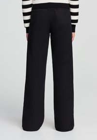 Czarne dżinsy z szerokimi nogawkami o gładkiej fakturze, z dwiema tylnymi kieszeniami i wysokim stanem. Stylizowane z paskowym swetrem na górze.