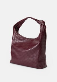Borsa tote in pelle intrecciata color bordeaux con forma morbida e disinvolta e un'unica tracolla annodata. Presenta una superficie testurizzata e un design minimalista.