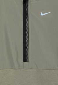 Pullover Nike de meio zíper em verde oliva. Apresenta um zíper preto, tecido texturizado e um logo azul claro no peito.