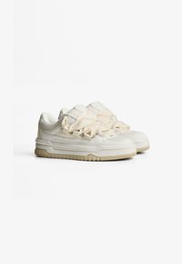 Crèmekleurige sneakers met gestructureerde overlay, gaasaccenten en dikke rubberen zolen. De veters hebben een uniek perzikachtig patroon.