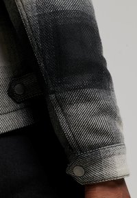 Schwarzer und weißer karierten Jackenärmel mit strukturierter Stoffoberfläche, Knopfdetail und kontrastierendem Farbverlauf von Schwarz zu Grau.