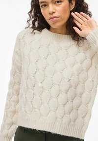 Pull crème tricoté avec un motif ovale en relief texturé, col rond et poignets côtelés. Bordure duveteuse à l'ourlet.