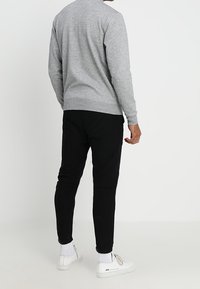 Šedý svetr s dlouhými rukávy, žebrovanými manžetami a lemem, kombinovaný s černými úzkými kalhotami a bílými teniskami. Neformální design a materiál.