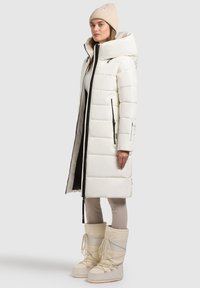 White puffer coat with a hood, featuring black zipper accents and a longline design. Paired with light-colored snow boots and leggings.