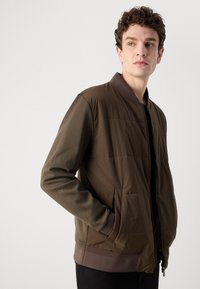 Lightweight bomber jacket featuring a two-tone design in dark brown. Textured fabric with a zip closure and side pockets. Ribbed cuffs.