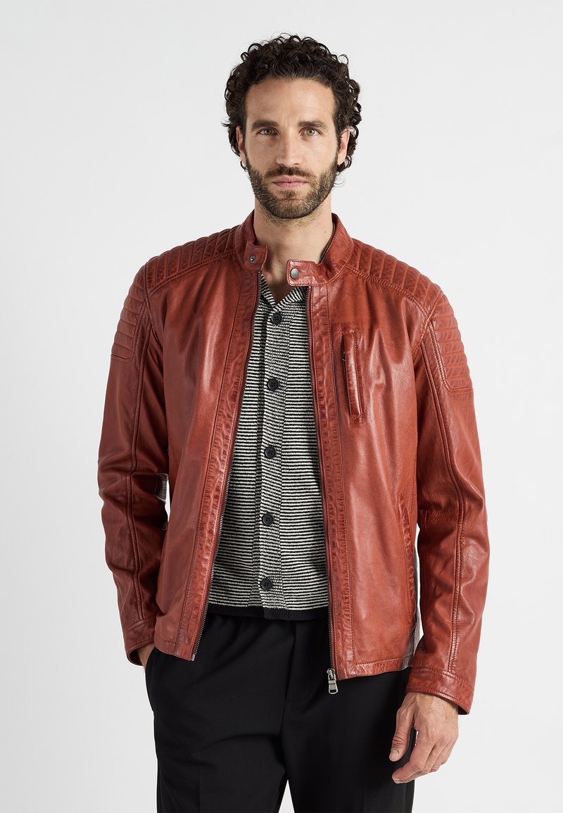 Veste en cuir rouge avec un col montant, des accents matelassés aux épaules et une fermeture éclair à l'avant. Assortie avec une chemise à rayures à boutons en dessous.