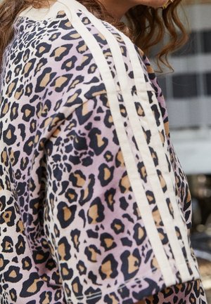 Zbliżenie na osobę noszącą koszulę z krótkim rękawem w panterkę z trzema białymi paskami na ramieniu i rękawie.