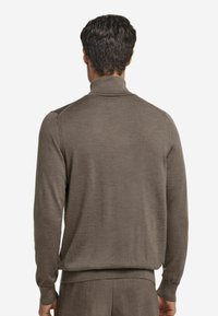 Brauner gestrickter Pullover mit hohem Kragen, langen Ärmeln und gerippten Bündchen. Weiche Textur und taillierte Passform. Wird mit passenden Hosen getragen.