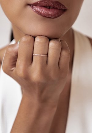 Rose gold ring with small embedded gems; worn on a hand with a natural skin tone, resting against the chin, showing smooth texture.