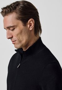 Czarny sweter na zamek błyskawiczny z wysokim kołnierzem, gładką fakturą i minimalistycznym wzorem, z akcentem w postaci srebrnego zamka.