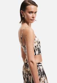 Top corto de estampado tie-dye en negro y beige con tirantes finos, tejido texturizado, diseño ajustado, combinado con pantalones a juego de estampado.