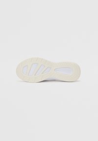 Sole of a white athletic shoe featuring a textured rubber bottom with multi-directional grooves and cutouts for grip and flexibility.