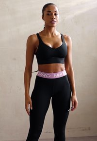 Crna sportska brusia i crne tajice s ružičastim Nike Pro pojasom. Glatka tkanina s prilagođenim dizajnom, koja prikazuje jednostavan logotip na tajicama.