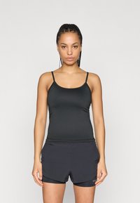 Débardeur de sport noir à fines bretelles, associé à un short foncé. Le tissu semble extensible et ajusté, parfait pour l'exercice.