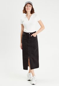 Jupe en denim noir avec fente sur le devant, taille haute et poches latérales. Associée à un polo blanc et des baskets blanches. Casquette grise portée.