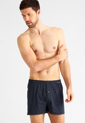 Marineblauwe boxershorts met een wit stippenpatroon, een elastische tailleband en een enkele knoopsluiting aan de voorkant. Zachte stofstructuur.