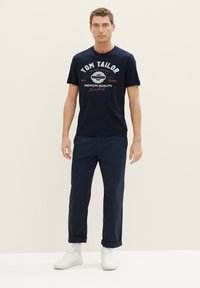 Mornarica T-shirt s grafičkim otiskom "Tom Tailor"; uparen s podvrnutim tamnim hlačama i bijelim tenisicama. Minimalistički dizajn, pamučni materijal.