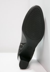 Chaussure en cuir noir avec un design matelassé et une semelle en caoutchouc texturé. Inclut une fermeture éclair décorative et un talon légèrement effilé.