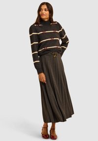 Maglione di lana a righe bianche e nere con dettagli a fiocco rosso, abbinato a una gonna maxi plissettata grigio scuro e scarpe con tacco lucide borgogna.