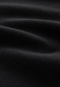 Primo piano di tessuto nero con una sottile trama diagonale a costine e morbide pieghe che creano ombre e luci delicate.