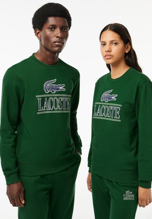 Sweatshirts en coton vert avec des poignets côtelés, ornés du logo Lacoste brodé et d'un design de crocodile. Associés à un pantalon de survêtement vert assorti.