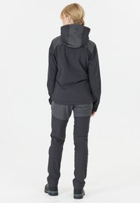 Vattentät svart utomhusjacka med huva, med grå accenter, zippered fickor och åtsittande svarta byxor, allt i matt finish.