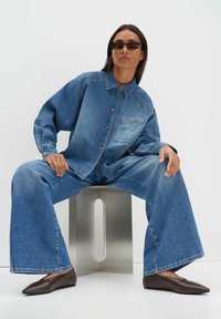 Jeanshemd und weit geschnittene Jeans in hellblau mit einer Brusttasche und Knopfleiste. Braune spitze Ballerinas vervollständigen das Outfit.