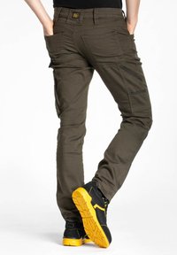 Pantalons cargo slim fit de couleur olive avec plusieurs poches et accents noirs, associés à des chaussures noires avec des semelles jaunes vives.