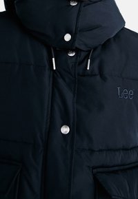 Svart puffjacka med hög krage, silverfärgade tryckknappar och präglad "Lee"-logotyp på bröstet. Slät, isolerad tyg med stora fickor.