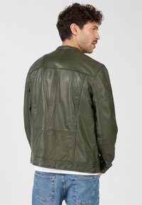 Olivengrüne Lederjacke mit glatter Textur, die horizontale und vertikale Nähte aufweist und einen einfachen runden Ausschnitt hat.