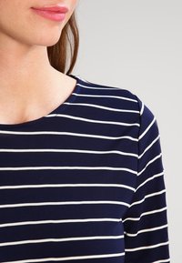 Mörkblå skjorta med vita horisontella ränder, rund halsringning och slät textur. Tyget verkar stretcha och sitta tight.