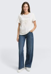 Wit T-shirt met korte mouwen en een bloemenprint, gecombineerd met wijde blauwe jeans en witte sneakers. Simpel, casual ontwerp.