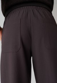 Pantaloni neri con vita elasticizzata e superficie liscia, dotati di due grandi tasche rettangolari sul retro.