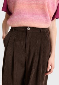 Pulover s gradijentom u ružičastoj i narančastoj boji, uparen s tamnosmešnim kord pantalonama s dugmetom i nabranim prednjim dijelom.
