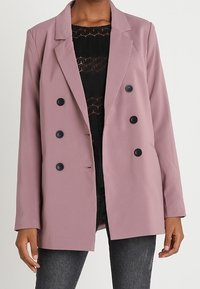 Dwurzędowa marynarka w kolorze mauve z czarnymi guzikami, z klapami i gładkiego materiału; zestawiona z fakturowanym czarnym topem i wąskimi dżinsami.