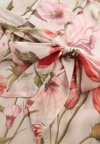 Robe en tissu floral avec des motifs botaniques roses, rouges et verts. Présente une taille nouée et des détails de boutons, fabriquée en matériau léger et texturé.
