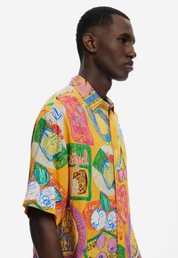 Kortærmet skjorte i klar gul med farverige, abstrakte frugt- og tekstmotiver. Lavet af letvægtstof med en afslappet pasform.