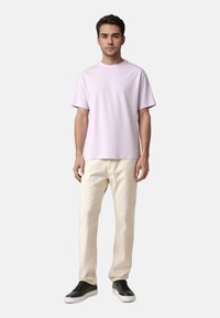 Helles lila T-Shirt mit kurzen Ärmeln, kombiniert mit weißen Hosen und schwarzen Sneakers. Glattes Material mit lockerem Schnitt. Minimalistisches Design.