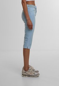 Capri in denim azzurro chiaro con vestibilità slim, vita media e piccoli spacchi laterali all'orlo, abbinati a sneakers grigie.