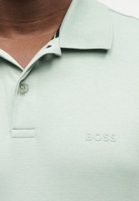 Φωτεινό πράσινο πόλο με γιακά και ένα κουμπί κλειστό, με το λογότυπο "BOSS" ανάγλυφο στο αριστερό στήθος.
