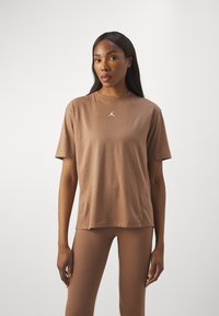 Camiseta de manga corta marrón hecha de material suave, con un pequeño logo blanco en el pecho. Corte recto con un cuello redondo.
