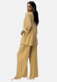 Outfit in tessuto marrone chiaro composto da un top largo e pantaloni a gamba ampia, abbinato a sandali con tacco di colore chiaro.
