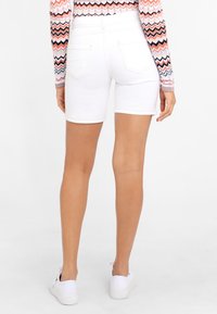 Weiße Denim-Shorts mit figurschmeichelndem Design, aufgerolltem Saum und zwei Gesäßtaschen, kombiniert mit weißen Sneakers.